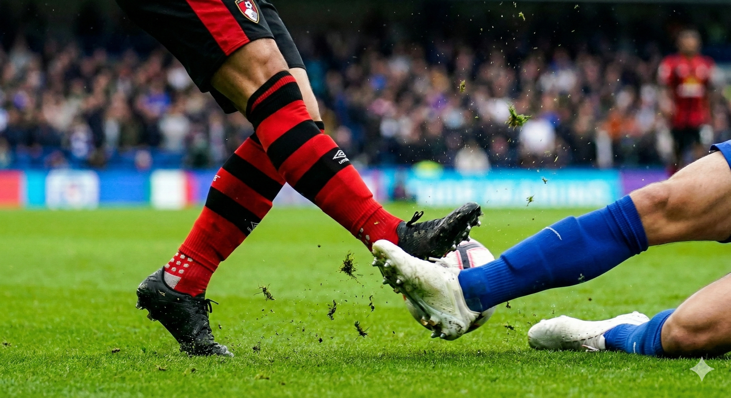 一张充满动感的赛场动作特写图,用于配合战术分析和比赛统计。视角贴近草地,捕捉球员激烈的拼抢瞬间。画面焦点在于脚部动作,一名穿着红黑球袜的球员正在运球或射门,另一名穿着蓝色球袜的防守球员试图拦截。草屑和水珠飞溅,展现出英超比赛的速度与力量感。背景略微虚化,突显前景的对抗细节,色彩饱和度高,光线处理细腻,呈现出专业的体育摄影风格。